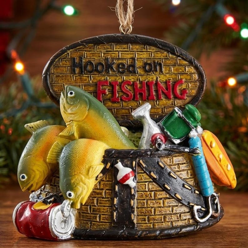 K&ouml;nnte beinhalten: Ein h&auml;ngendes Ornament in Form eines gelben Ziegelkorbs mit dem Text Hooked on FISHING. Es zeigt zwei gelbe Fische, eine rote Getr&auml;nkedose, eine rot-wei&szlig;e Angelpose, ein silbernes Werkzeug, einen gr&uuml;nen Beh&auml;lter und einen blauen Angelrutengriff.