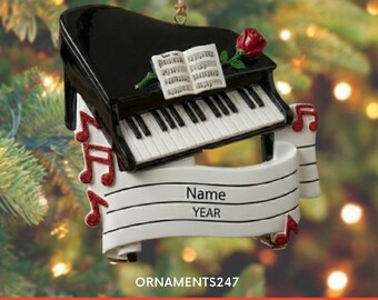 Peut inclure: Une décoration en forme de piano à queue noir avec des touches blanches, une rose rouge et un livre de musique ouvert. Une bannière blanche avec des lignes noires et le texte Name et YEAR est fixée, ornée de notes de musique à paillettes rouges.