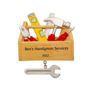 May include: A wooden toolbox ornament with a yellow level, a red screwdriver, a silver hammer, a pair of pliers, and a silver wrench hanging from the bottom. The toolbox is labeled "Ben's Handyman Services 2022".