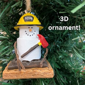 Puede incluir: Un adorno navideño 3D con forma de muñeco de nieve de malvavisco que lleva un gorro de bombero amarillo con la palabra "FIRE" en él. El muñeco de nieve sostiene un hacha roja y está sentado en una galleta graham.