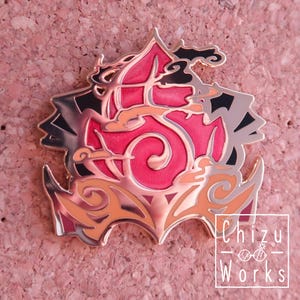 May include: A decorative pin with a stylized design in shades of pink, orange, and silver. The pin features a central swirling pattern and is outlined in a metallic finish. The text "Chizu Works" is visible on the bottom right.