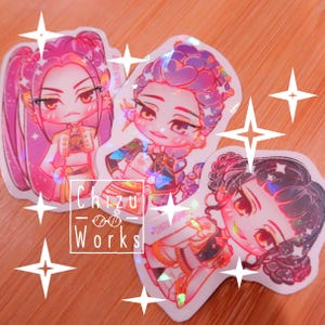 Op de afbeelding: Drie holografische stickers met anime-stijl illustraties van vrouwen met gedetailleerde kapsels en outfits. De stickers hebben een glanzende, iriserende afwerking en zijn geplaatst tegen een warme, houten achtergrond. De tekst "Chizu Works" is zichtbaar.