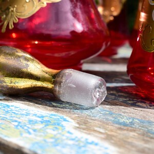 May include: A gold and clear glass bottle stopper with a bulbous shape. The stopper is lying on a weathered wooden surface.