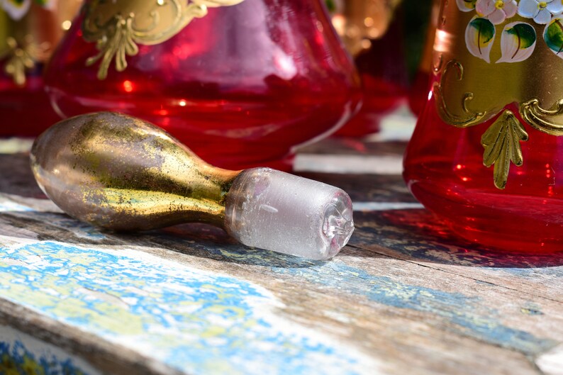 May include: A gold and clear glass bottle stopper with a bulbous shape. The stopper is lying on a weathered wooden surface.