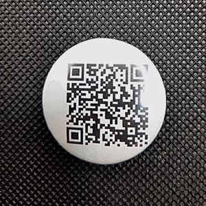 May include: A white round button with a black and white QR code printed on it.
