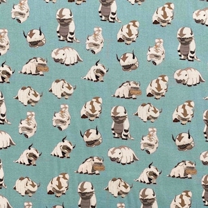 Peut inclure: Un tissu bleu avec un motif r&eacute;p&eacute;t&eacute; de bisons de dessin anim&eacute; blancs et bruns. Les bisons sont dans diverses poses, y compris debout, assis et couch&eacute;s.