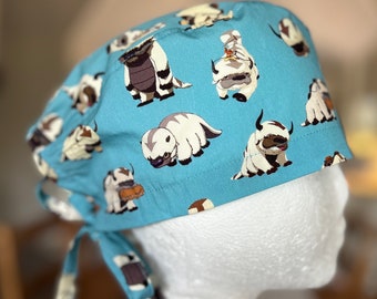 May include: A blue scrub hat with a white tie, featuring a repeating pattern of white yak-like creatures on a light blue background.