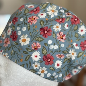 Puede incluir: Un gorro quirúrgico azul con un estampado floral en rojo, rosa, blanco y verde. El gorro presenta un diseño repetido de flores y hojas. Este gorro está diseñado para ser usado en entornos médicos o de atención médica.