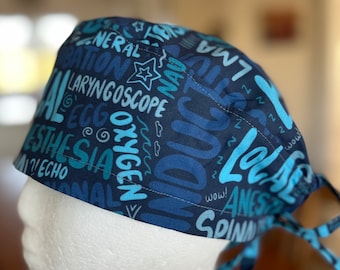 May include: Blue and teal scrub hat with a pattern of medical terms, including 'General Anesthesia', 'Laryngoscope', 'Oxygen', 'LMA', 'EKG', 'Echo', 'Spinal', 'Anesthesia', 'Let's Go', 'Zzz', and 'Wow!'