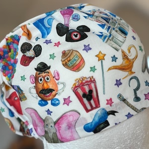Op de afbeelding: Witte chirurgische scrubcap met kleurrijke illustraties van Disney-personages en iconen. De cap heeft afbeeldingen van Mickey Mouse, Mr. Potato Head, Dumbo en een magische lamp, onder andere. Het ontwerp bevat sterren en een honingpot.