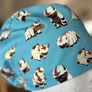 Peut inclure: Un bonnet de chirurgien bleu avec un motif r&eacute;p&eacute;t&eacute; de bisons de dessin anim&eacute; blancs et bruns. Les bisons sont dans diff&eacute;rentes poses, y compris debout, marchant et couch&eacute;s.