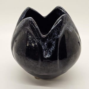 May include: Black ceramic flower pot with a white glaze. The pot is shaped like a tulip and has a wide opening.
