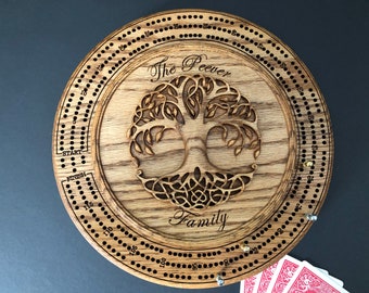 May include: A circular wooden cribbage board featuring a laser-engraved tree of life design in the center. The text "The Peever Family" is engraved above and below the tree. The board includes numbered scoring tracks, start and finish labels.