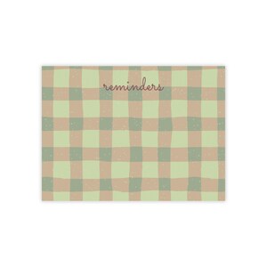 Peut inclure: Un bloc-notes rectangulaire avec un motif à carreaux dessiné à la main, alternant des nuances de vert sauge et de beige. La surface est parsemée de petits points blancs. Le mot "reminders" est imprimé en cursive brun foncé.