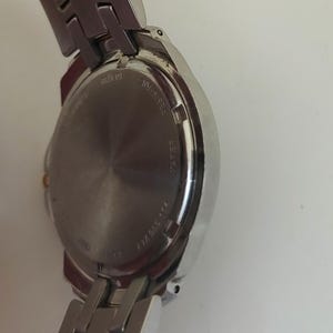 K&ouml;nnte beinhalten: Nahaufnahme einer silberfarbenen Armbanduhr. Die Uhr hat ein rundes Zifferblatt und ein Edelstahlarmband. Die R&uuml;ckseite der Uhr ist sichtbar, mit Angaben zur Wasserdichtigkeit. Die Uhr hat ein klassisches Design.