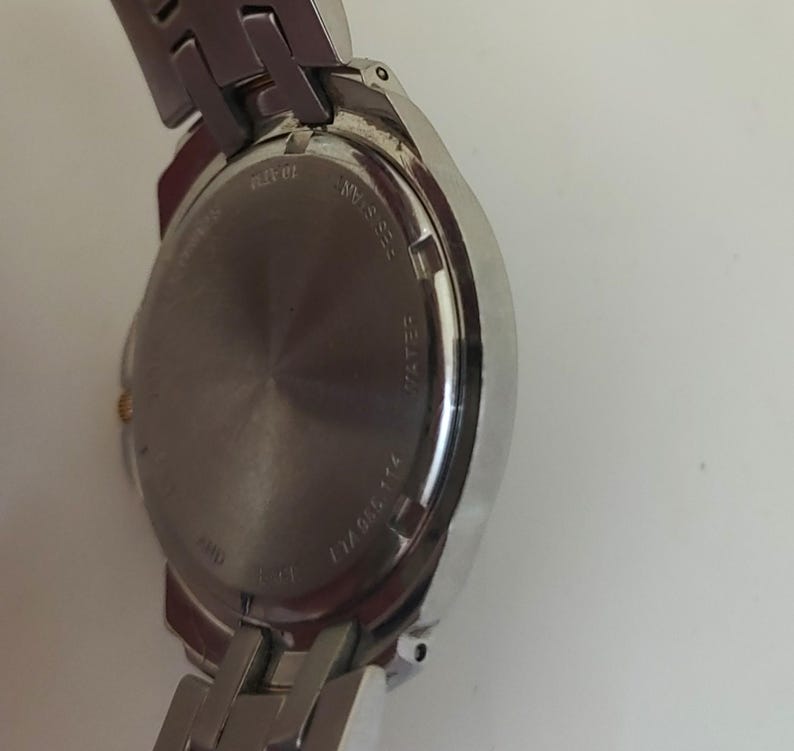 K&ouml;nnte beinhalten: Nahaufnahme einer silberfarbenen Armbanduhr. Die Uhr hat ein rundes Zifferblatt und ein Edelstahlarmband. Die R&uuml;ckseite der Uhr ist sichtbar, mit Angaben zur Wasserdichtigkeit. Die Uhr hat ein klassisches Design.