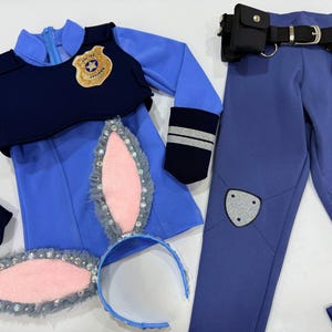 May include: A blue and navy police officer costume set. The set includes a long-sleeved top with a badge, pants, a utility belt, and bunny ears. The bunny ears are gray with pink centers and embellished with rhinestones.