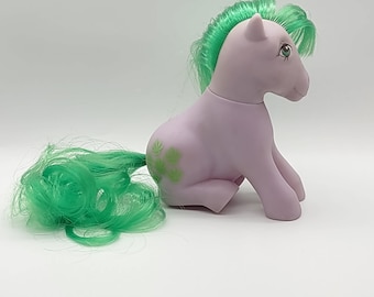 May include: A purple My Little Pony with green hair and a green tail. The pony has a green clover design on its side.