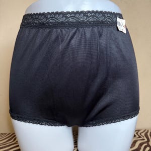 Op de afbeelding: Zwarte nylon onderbroek met een kanten rand. De onderbroek heeft een label aan de tailleband.