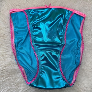 May include: Teal satin underwear with pink trim and a small pink bow. The underwear has a high-waisted design with a shiny, smooth texture. The edges are trimmed with a delicate pink lace.