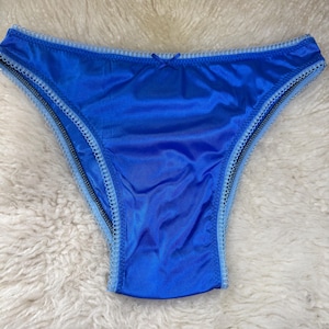May include: Vibrant blue underwear with a satin sheen. The edges are trimmed with light blue lace and a small bow. A black zipper-like detail runs along the edges of the underwear.