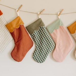 May include: Five Christmas stockings suspended from a string, each with a unique pattern and colour. The stockings have scalloped tops and are made of fabrics like stripes, polka dots, and gingham.