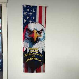 May include: A patriotic banner featuring an American flag design with a detailed illustration of an eagle's head. The banner includes the text "Happy 250th Anniversary of America" in yellow lettering, celebrating a significant milestone.
