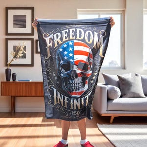 May include: A black blanket featuring a skull design with the American flag incorporated into the skull's design. The words "FREEDOM" and "INFINITY" are displayed in gold lettering. The blanket also includes the text "250" and other text.