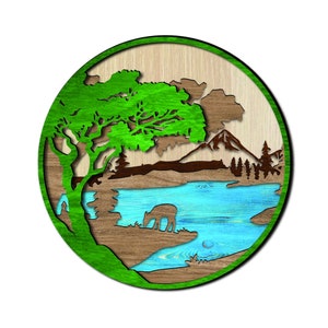 May include: A round wooden wall art piece featuring a green tree, brown mountains, and a blue lake. The lake has a small stream flowing out of it. The piece is crafted from wood and has a rustic appearance.