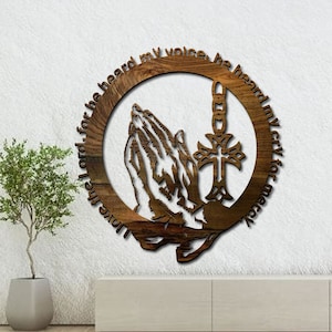 May include: Wooden wall decor with a circular design featuring a cross and praying hands. The text around the circle reads "Love the Lord for he heard my voice, he heard my cry for mercy."