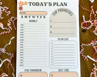 May include: A printable daily planner with a peach background and floral accents. The planner includes sections for "Today's Plan", "Top Priorities", "To Do List", "For Tomorrow", and "Self Care".