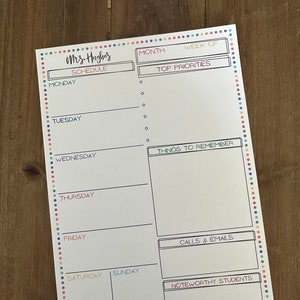 May include: A white weekly planner with a colorful dotted border and a row of colored pens at the bottom. The planner includes sections for each day of the week, top priorities, and notes. The name "Mrs. Hughes" is at the top.