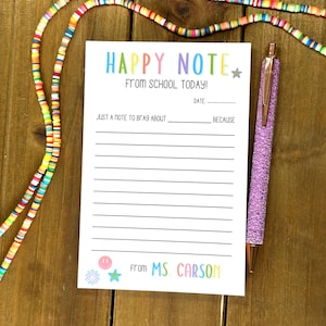 May include: A white notepad with the text "HAPPY NOTE" in rainbow colors, a matching pen, and a colorful beaded necklace. The notepad reads "From School Today!" and "From Ms. Carson."