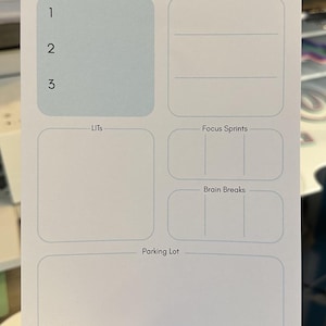 May include: A white planner page with the text "What Will My Future Self Thank Me For?" and sections for MITs, Personal MITs, LITs, Focus Sprints, Brain Breaks, and a Parking Lot. The page is held by a hand.