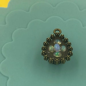 Op de afbeelding: Een kleine, ronde, bronzen hanger met een ontwerp van vijf iriserende opaalstenen die in een cirkelvormig frame zijn gezet.