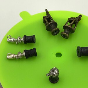 May include: A green silicone mat with six small metal charms. The charms are in the shape of a lantern, a spool of thread, and a small decorative object.