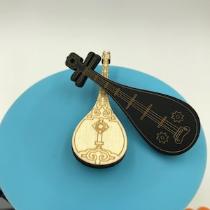 May include: Two wooden Chinese pipas, one black and one natural wood with gold detailing, on a blue surface.