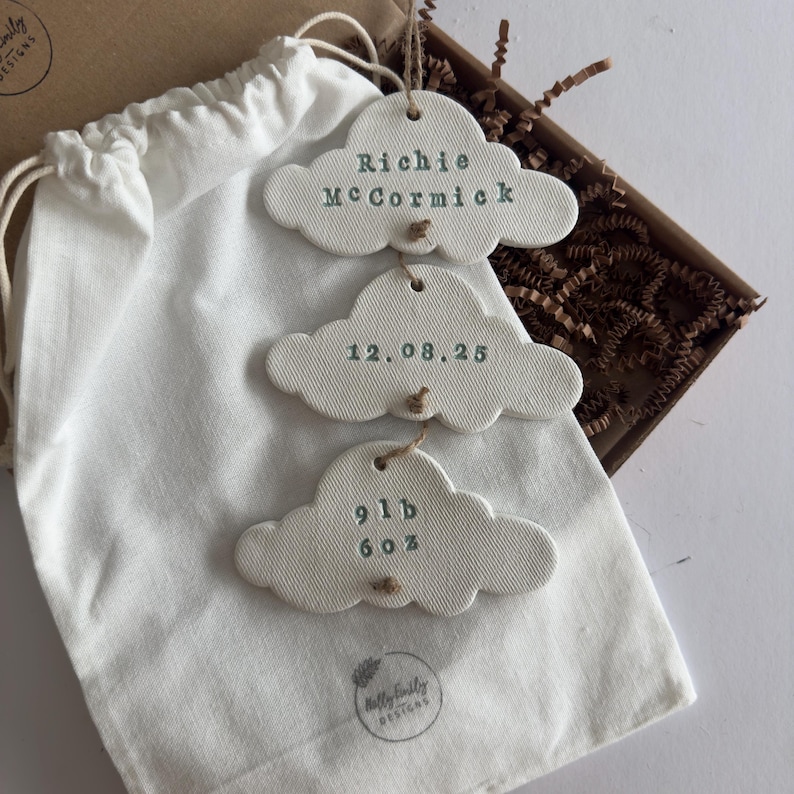 personalised Clay cloud wall hanging keepsake decoration ornament. three clouds attached to each other with twine for nursery wall art. First cloud has baby’s name, middle cloud baby weight and third cloud birth date. handpainted in choice of colour, with cotton gift bag option
