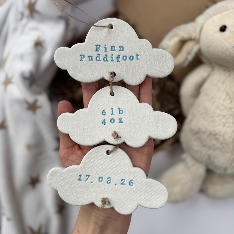 personalised Clay cloud wall hanging keepsake decoration ornament. three clouds attached to each other with twine for nursery wall art. First cloud has baby’s name, middle cloud baby weight and third cloud birth date. handpainted in choice of colour