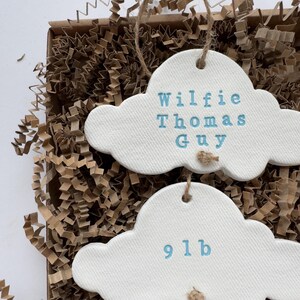 personalised Clay cloud wall hanging keepsake decoration ornament. three clouds attached to each other with twine for nursery wall art. First cloud has baby’s name, middle cloud baby weight and third cloud birth date. handpainted in choice of colour