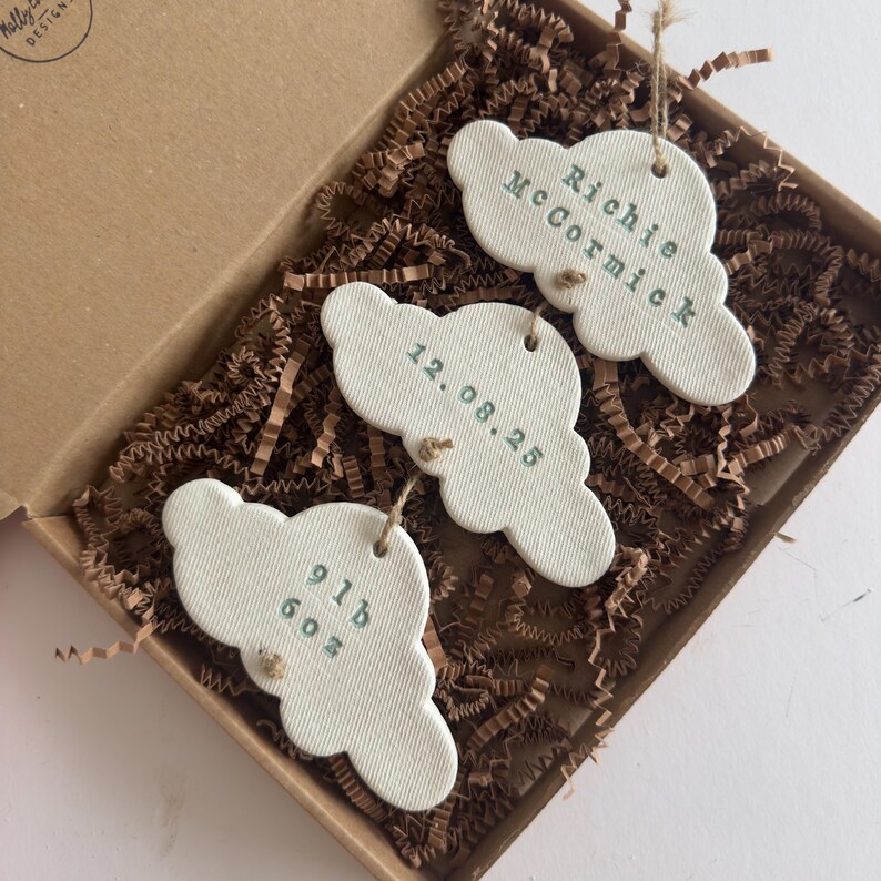 personalised Clay cloud wall hanging keepsake decoration ornament. three clouds attached to each other with twine for nursery wall art. First cloud has baby’s name, middle cloud baby weight and third cloud birth date. handpainted in choice of colour