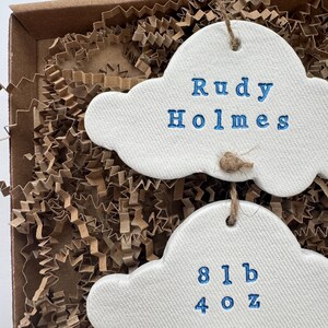 personalised Clay cloud wall hanging keepsake decoration ornament. three clouds attached to each other with twine for nursery wall art. First cloud has baby’s name, middle cloud baby weight and third cloud birth date. handpainted in choice of colour