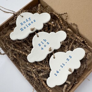 personalised Clay cloud wall hanging keepsake decoration ornament. three clouds attached to each other with twine for nursery wall art. First cloud has baby’s name, middle cloud baby weight and third cloud birth date. handpainted in choice of colour