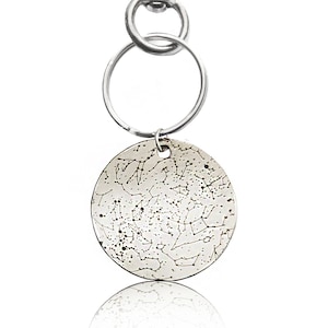 May include: Silver keychain with a round charm featuring a constellation design. The charm is attached to a silver split ring and a silver lobster clasp.