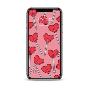 May include: A pink iPhone with a lock screen displaying the time 12:35 and the date Sunday, May 1. The background is a pattern of red heart-shaped lollipops on pink.