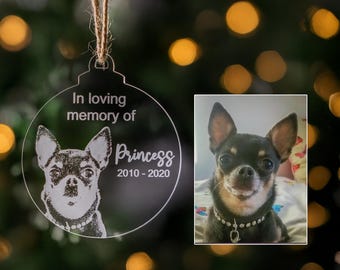 May include: Clear acrylic Christmas ornament with a dog portrait and the text "In loving memory of Princess 2010-2020." The ornament is round with a string for hanging. A photo of the dog is next to the ornament. The dog is black and brown with a jeweled collar.