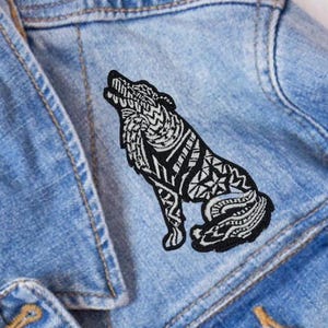 May include: A black and white embroidered wolf patch with a tribal design. The patch is sewn onto a blue denim jacket.