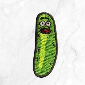 May include: Embroidered patch featuring a green pickle with a surprised expression and a black outline. The pickle has a yellow center and a red mouth. The patch is likely for clothing or accessories.