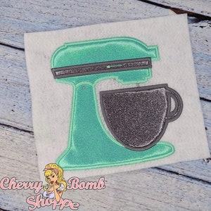 Puede incluir: Aplicación de batidora de pie turquesa con cuenco y detalles plateados con purpurina. El diseño está sobre un fondo blanco. El texto "Cherry Bomb Shoppe" está en la esquina inferior izquierda.