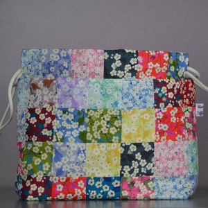 May include: A colourful patchwork drawstring bag with a white cord and tassel. The bag is made of fabric with a floral pattern.